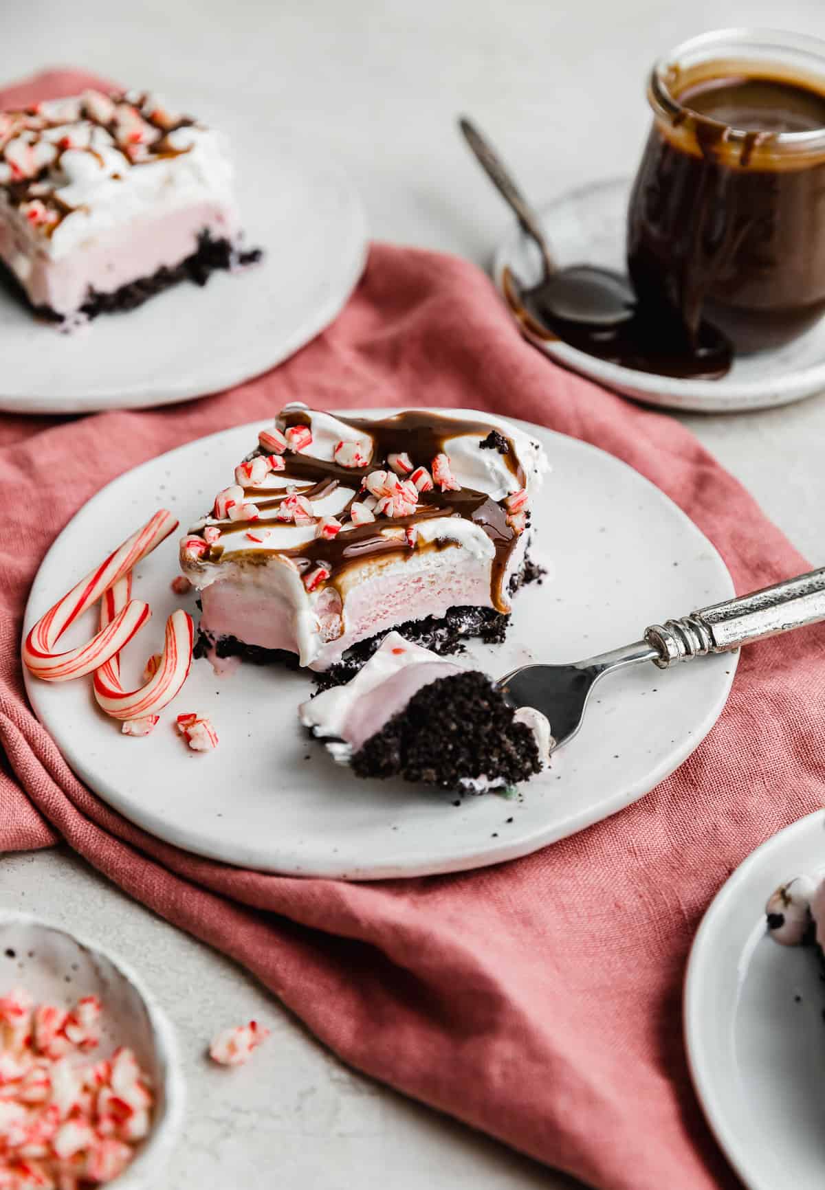 A slice of Christmas Ice Cream Cake on a white plate; oreo crust, peppermint ice cream, and whipped cream topping.