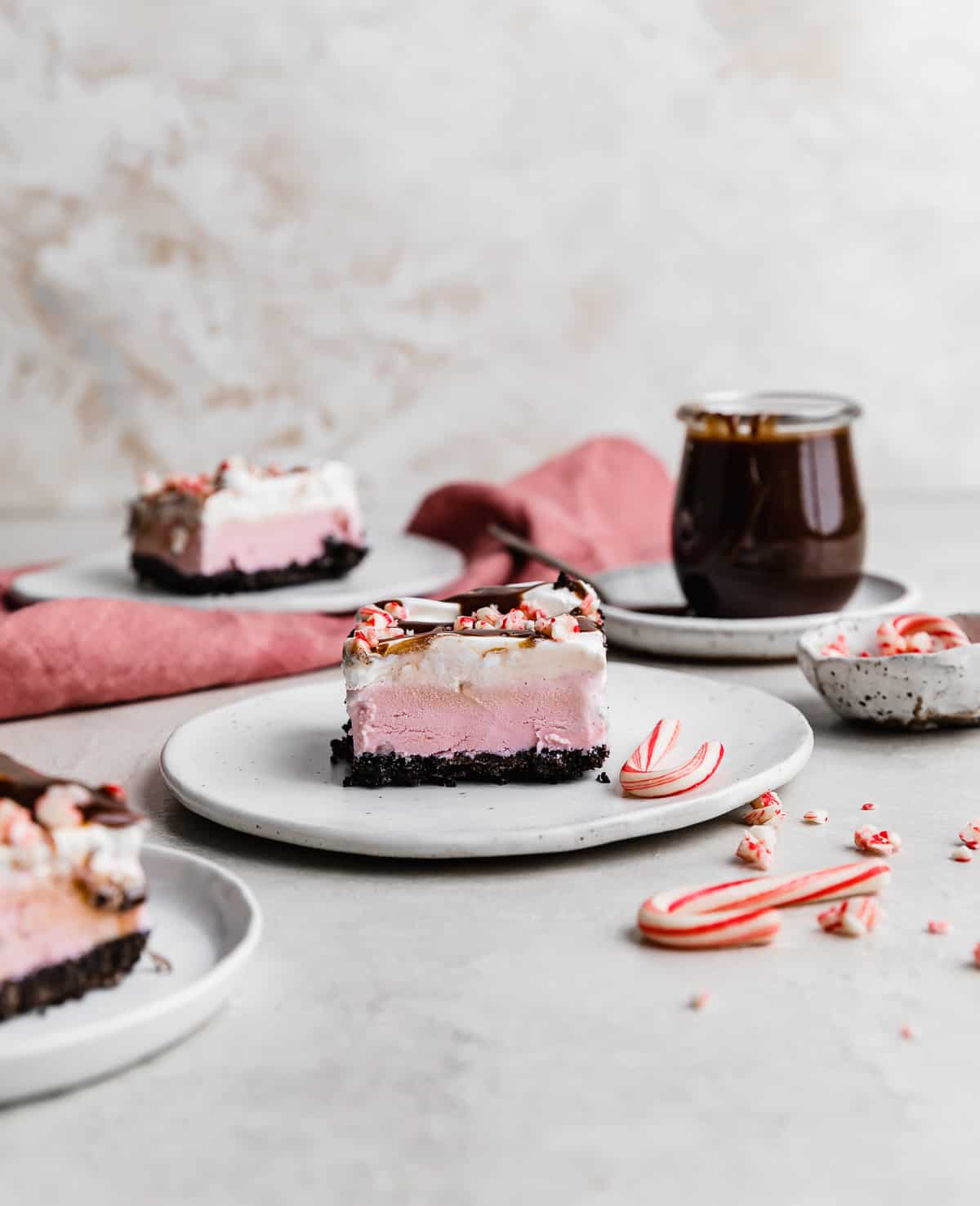 A slice of Christmas Ice Cream Cake on a white plate with a jar of hot fudge in the background.