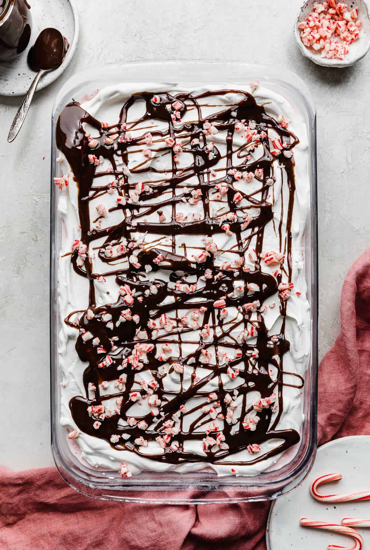 Hot fudge and crushed candy canes sprinkled overtop a whip cream topped peppermint Christmas Ice Cream Cake.