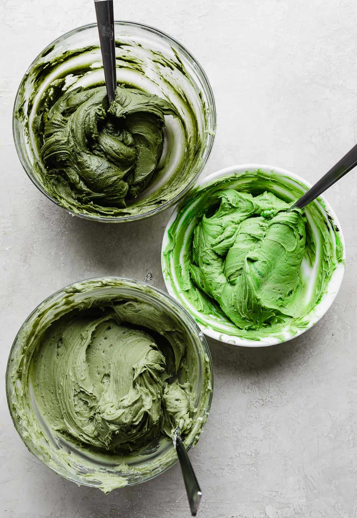 Three bowls of differing shades of green buttercream, for making christmas trees on a Christmas Tree Cake.