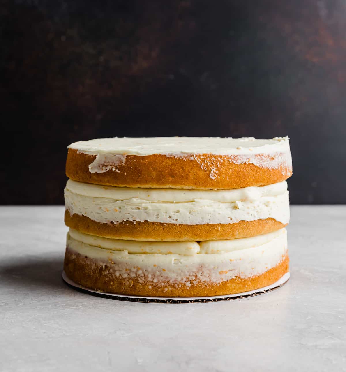 A three layered naked cake against a brown background.