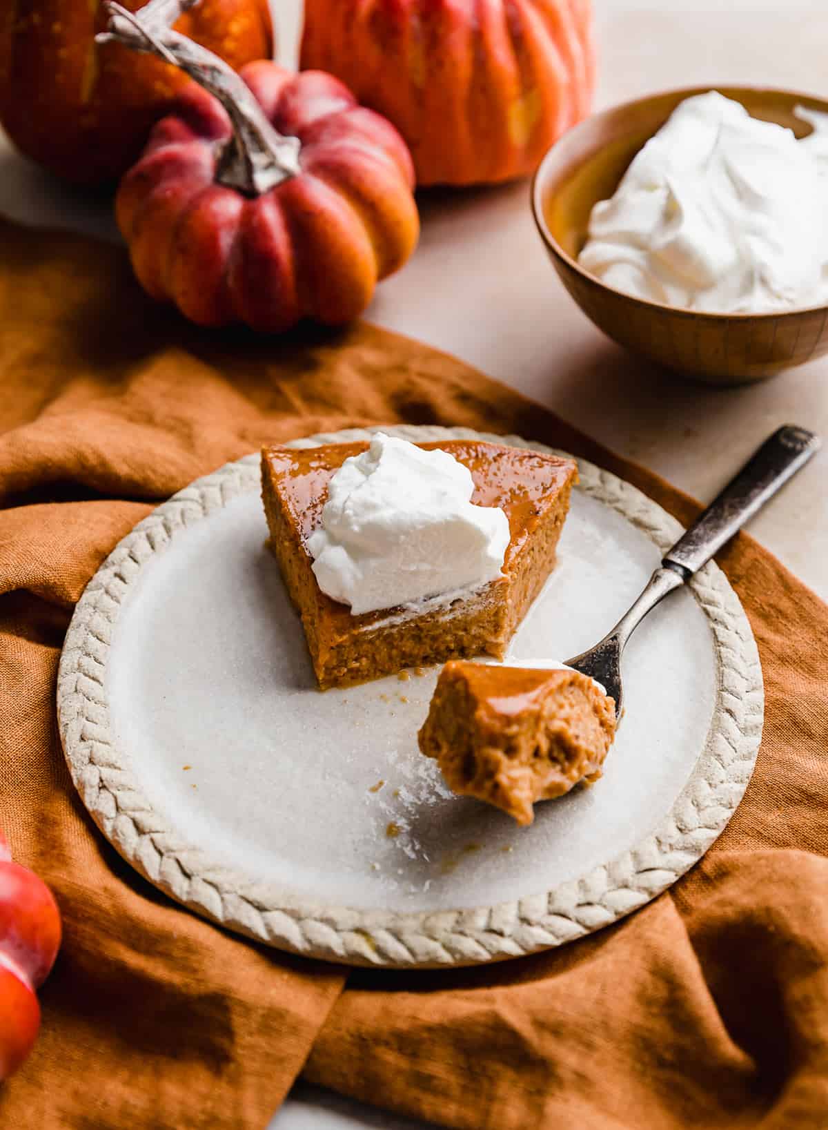 A slice of Crustless Pumpkin Pie on a plate, dolloped with whipped cream.