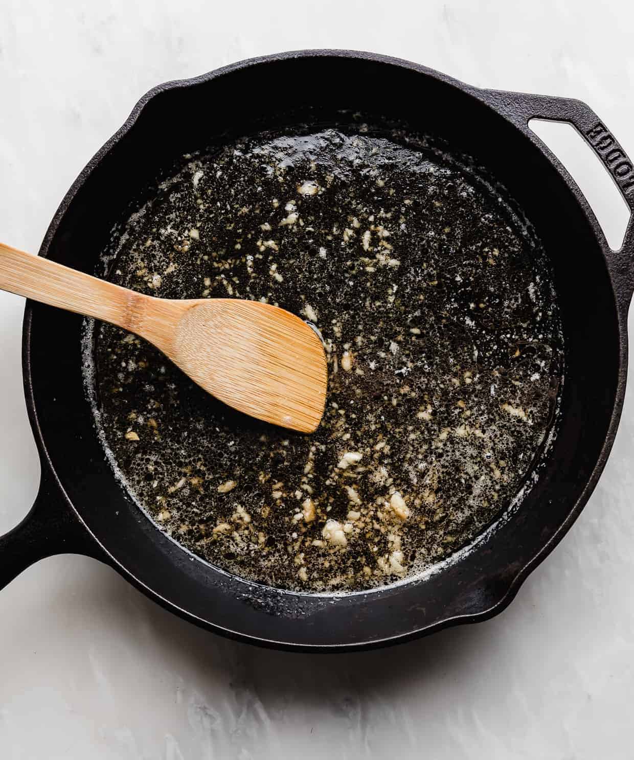 An overhead photo of a light colored sauce in a black skillet, to make Honey Garlic Baked Salmon.