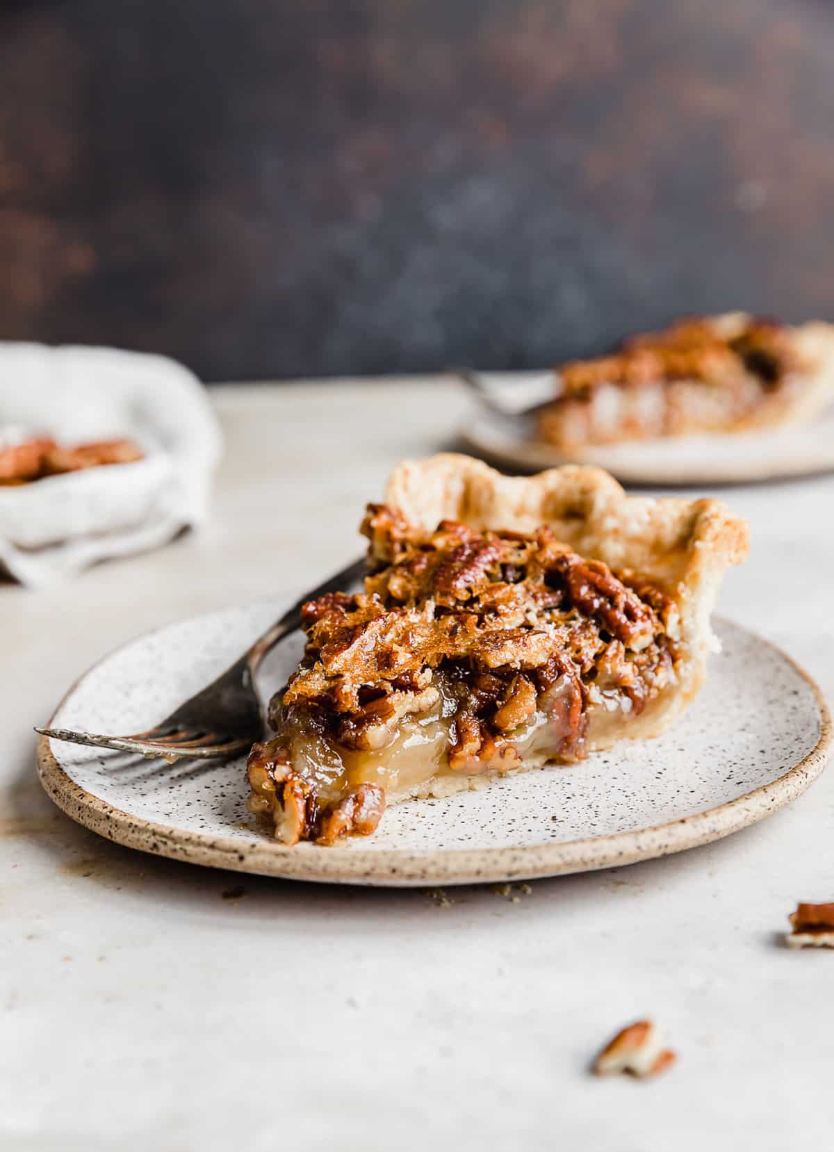 A slice of Southern Pecan Pie on a white plate with a fork to the side of the pie.