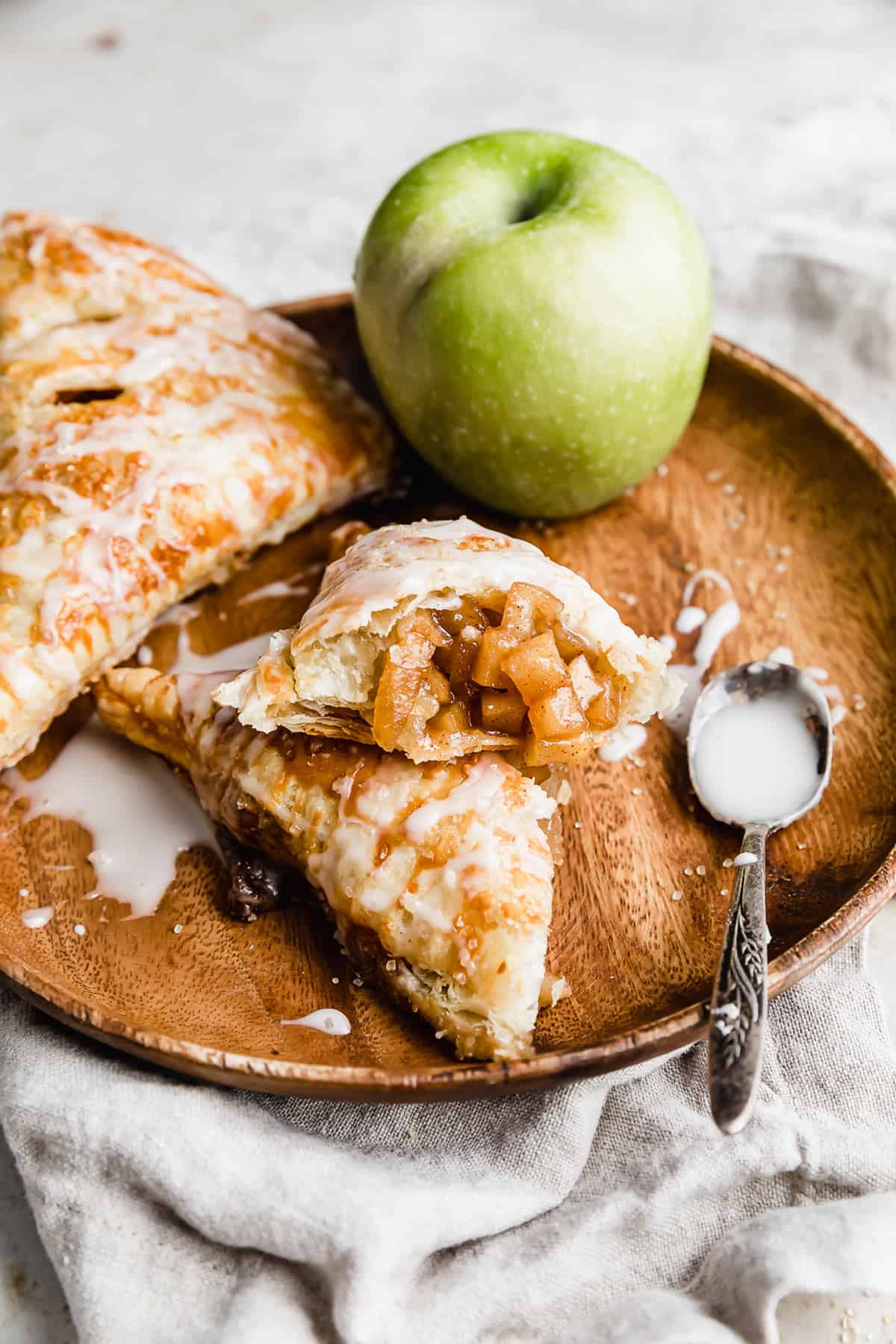 A Puff Pastry Apple Turnover cut in half, on a brown plate, topped with a glaze. 