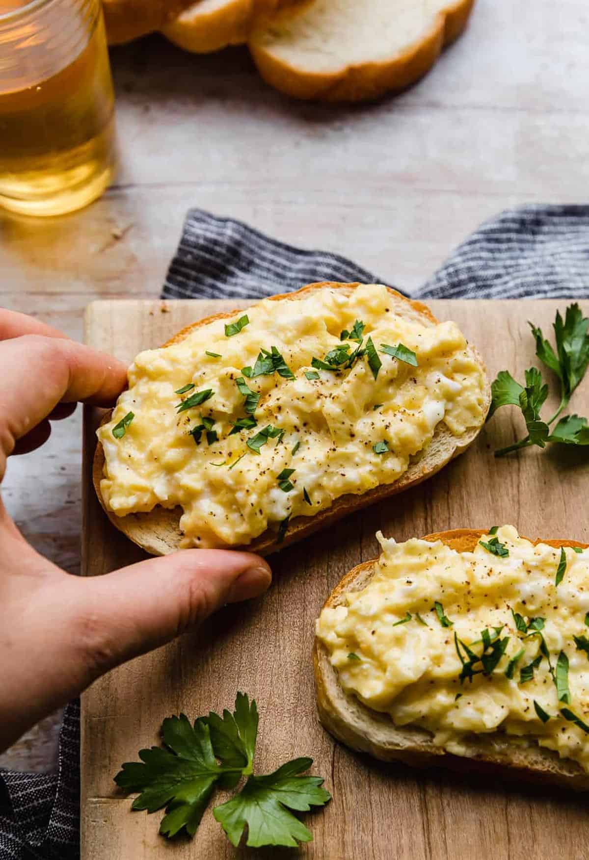 A hand holding a slice of toast that is topped with cheesy scrambled eggs.