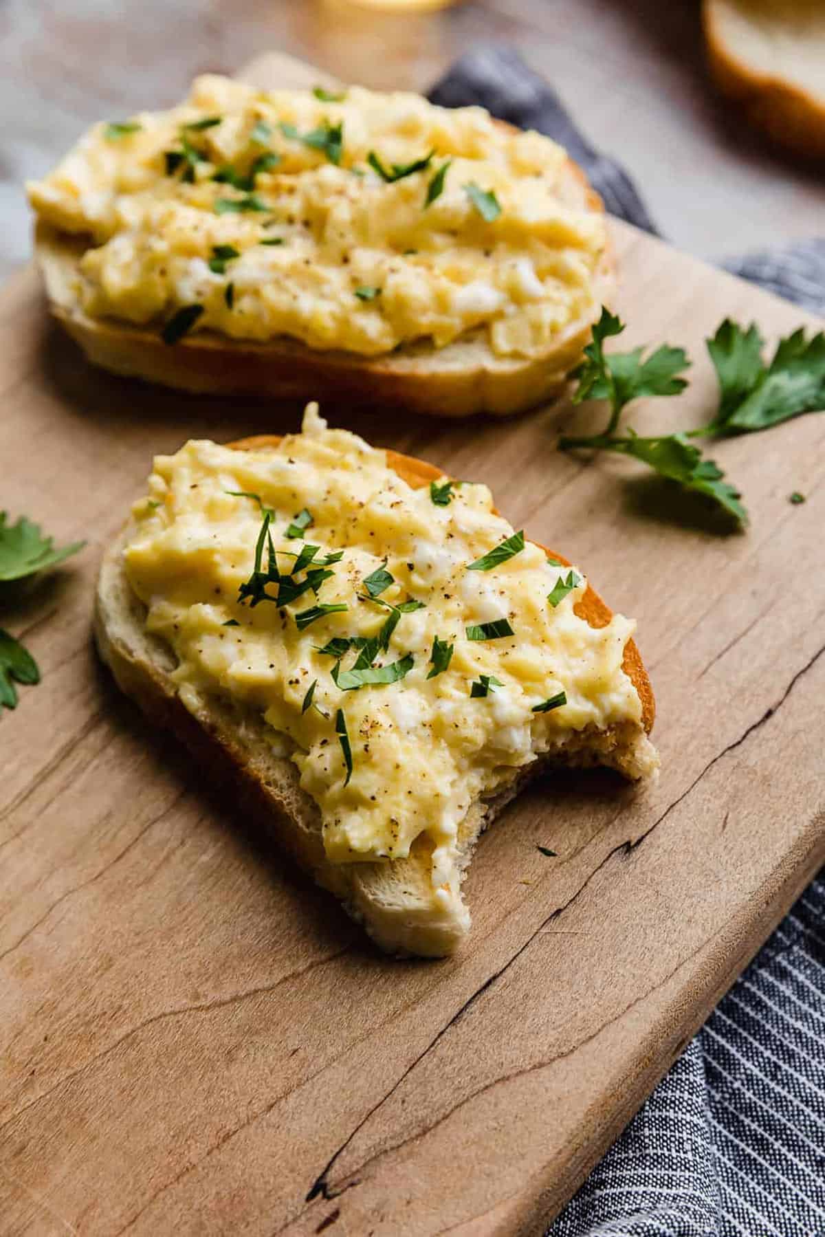  A piece of bread topped with scrambled eggs that's topped with parsley.