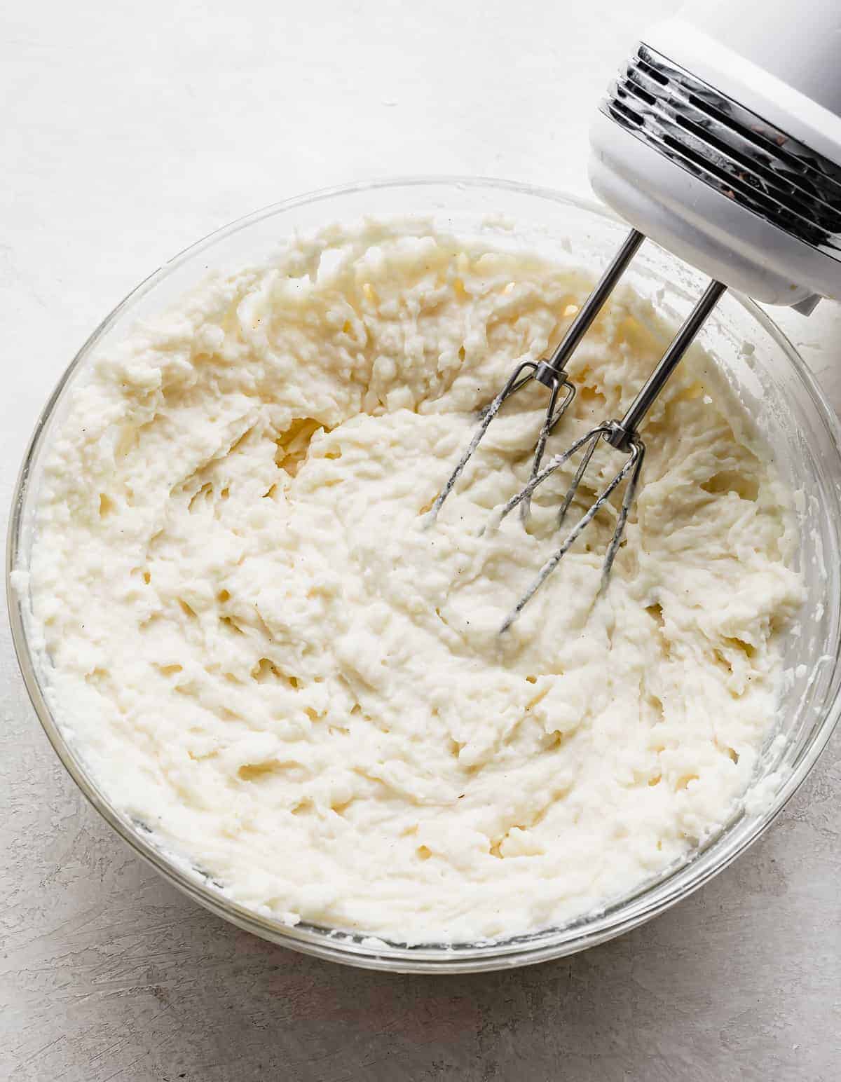 A hand mixer beating the Twice Baked Potatoes with Cream Cheese mixture in a glass bowl.