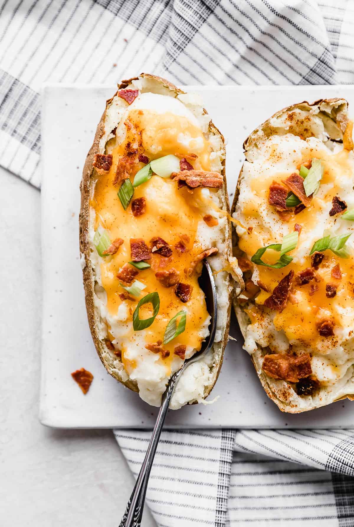 A Twice Baked Potatoes with Cream Cheese topped with orange cheese and crispy bacon, on a white plate.