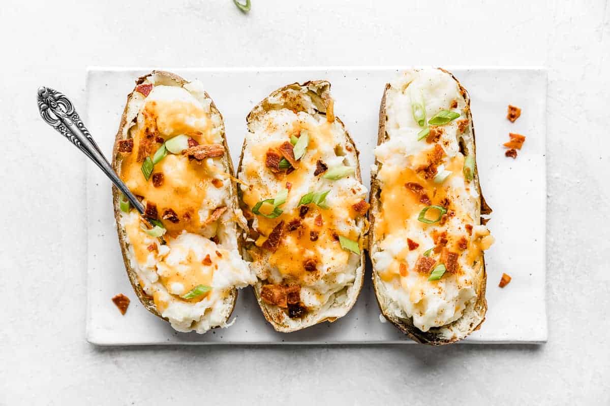 Three Twice Baked Potatoes with Cream Cheese topped with bacon and green onions, resting on a white plate.