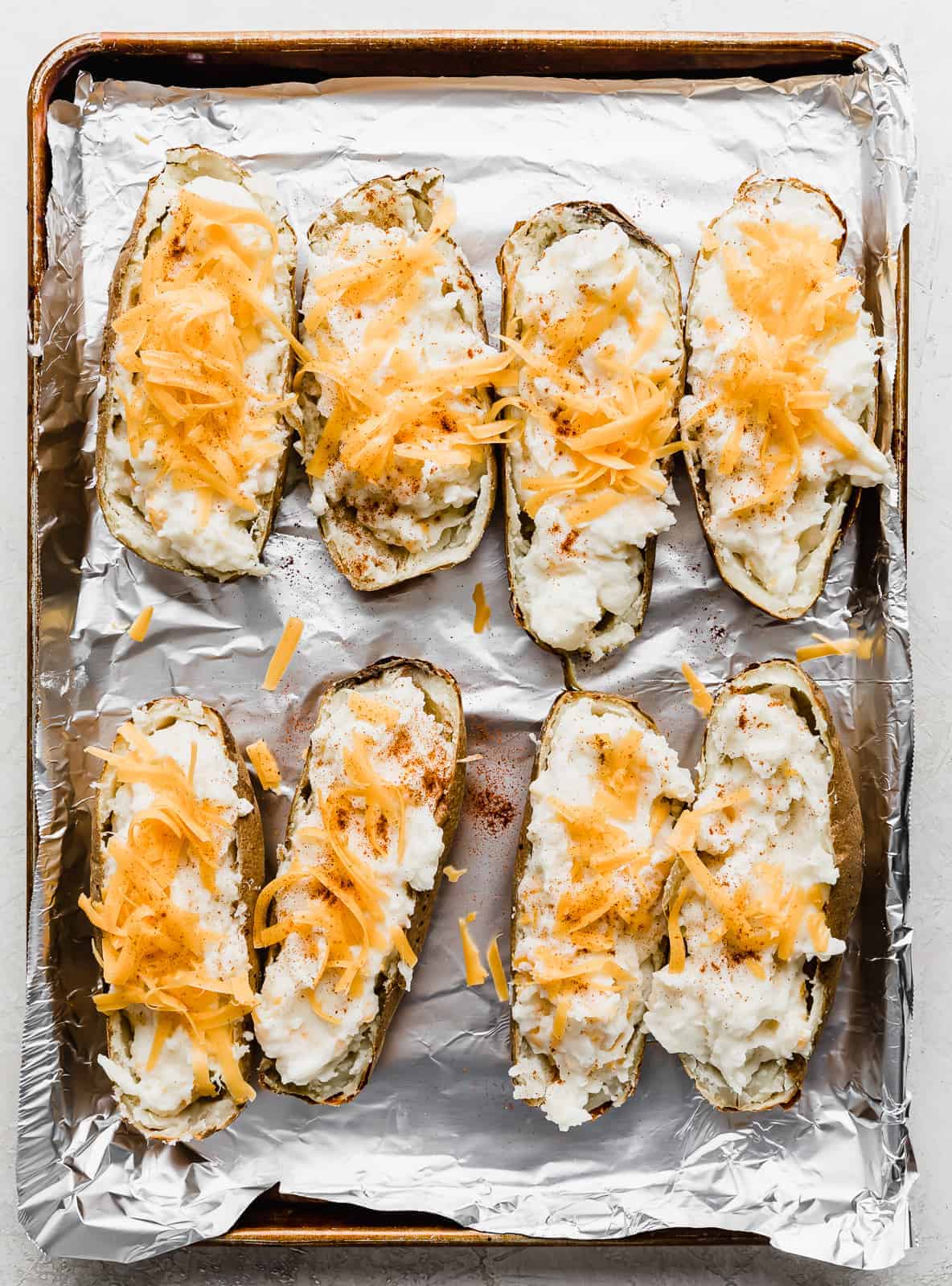 Twice Baked Potatoes topped with shredded cheddar cheese.
