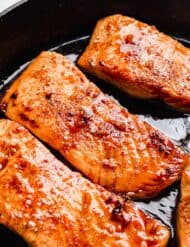 A close up photo of Honey Garlic Baked Salmon filets in a black skillet.