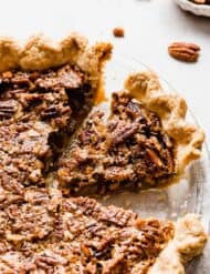 A pecan pie on a white background with pecan pieces in the background.