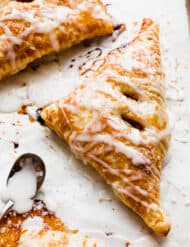 A glazed Puff Pastry Apple Turnover on a white parchment paper.