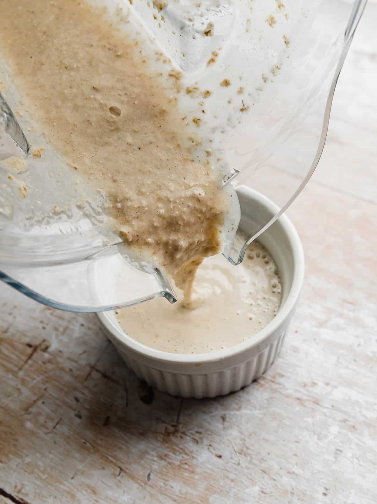 Baked oats mixture being poured into a white ramekin from a blender.