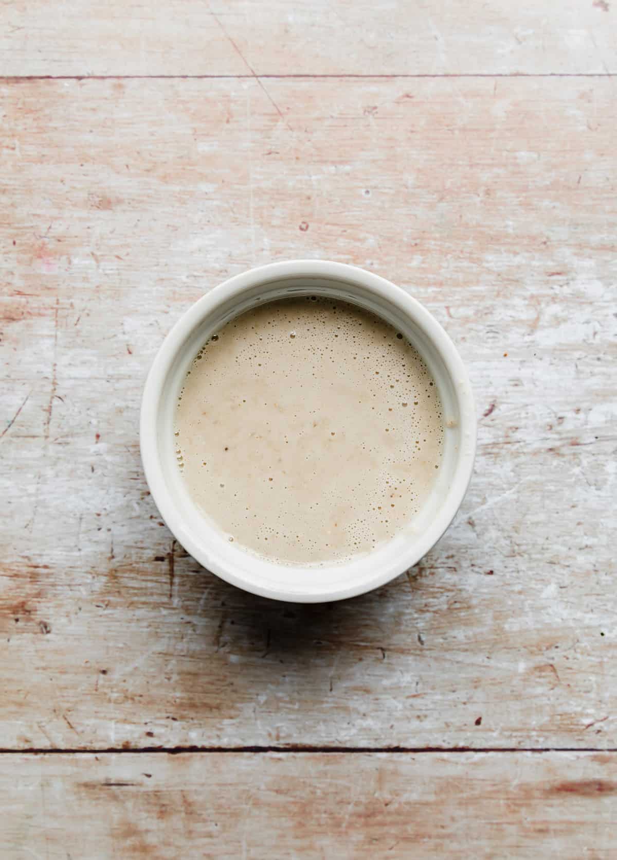 A tan colored oat liquid mixture in a white ramekin on a light brown wooden background.