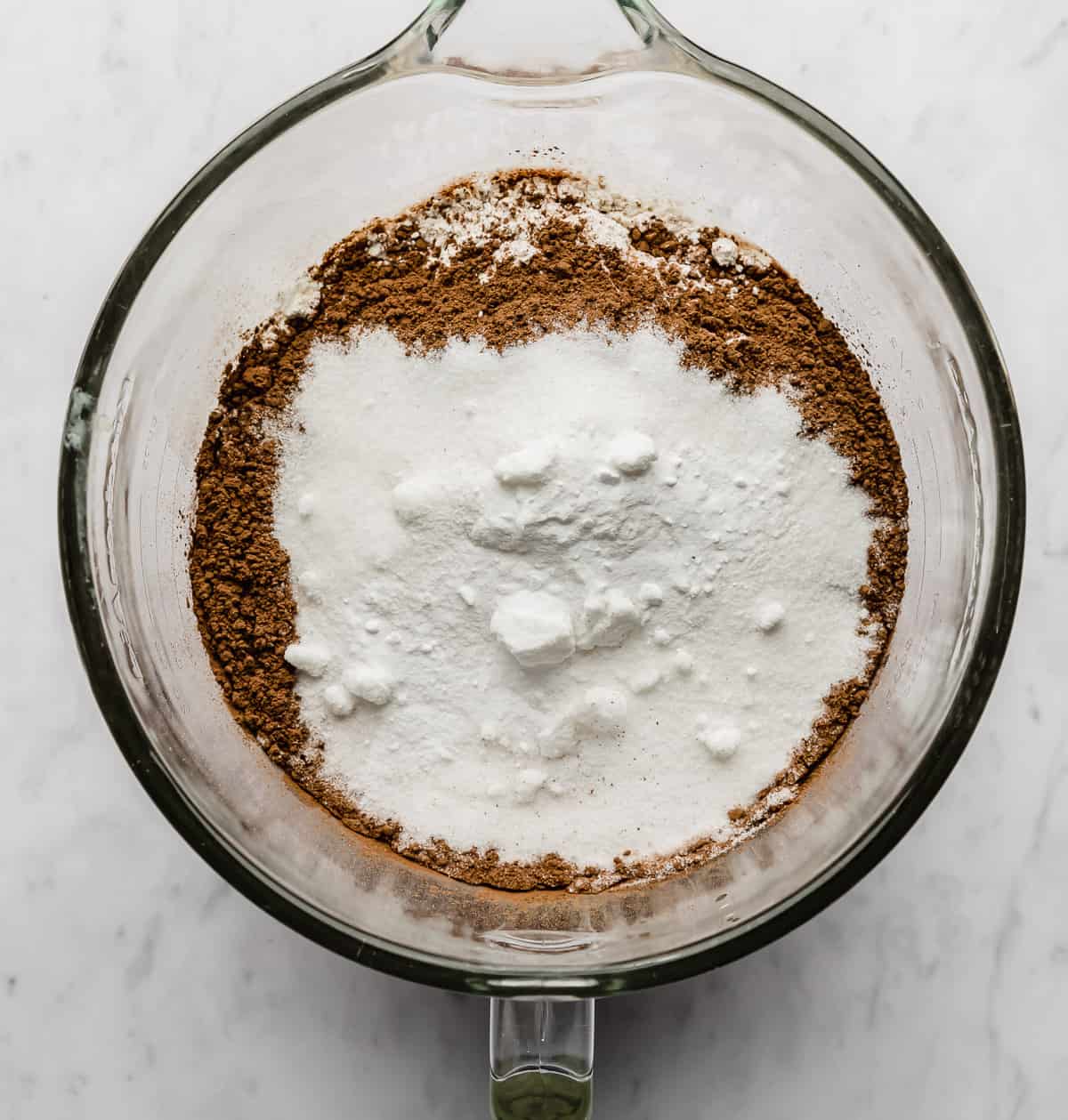 A glass mixing bowl with cocoa, sugar, and flour in it.
