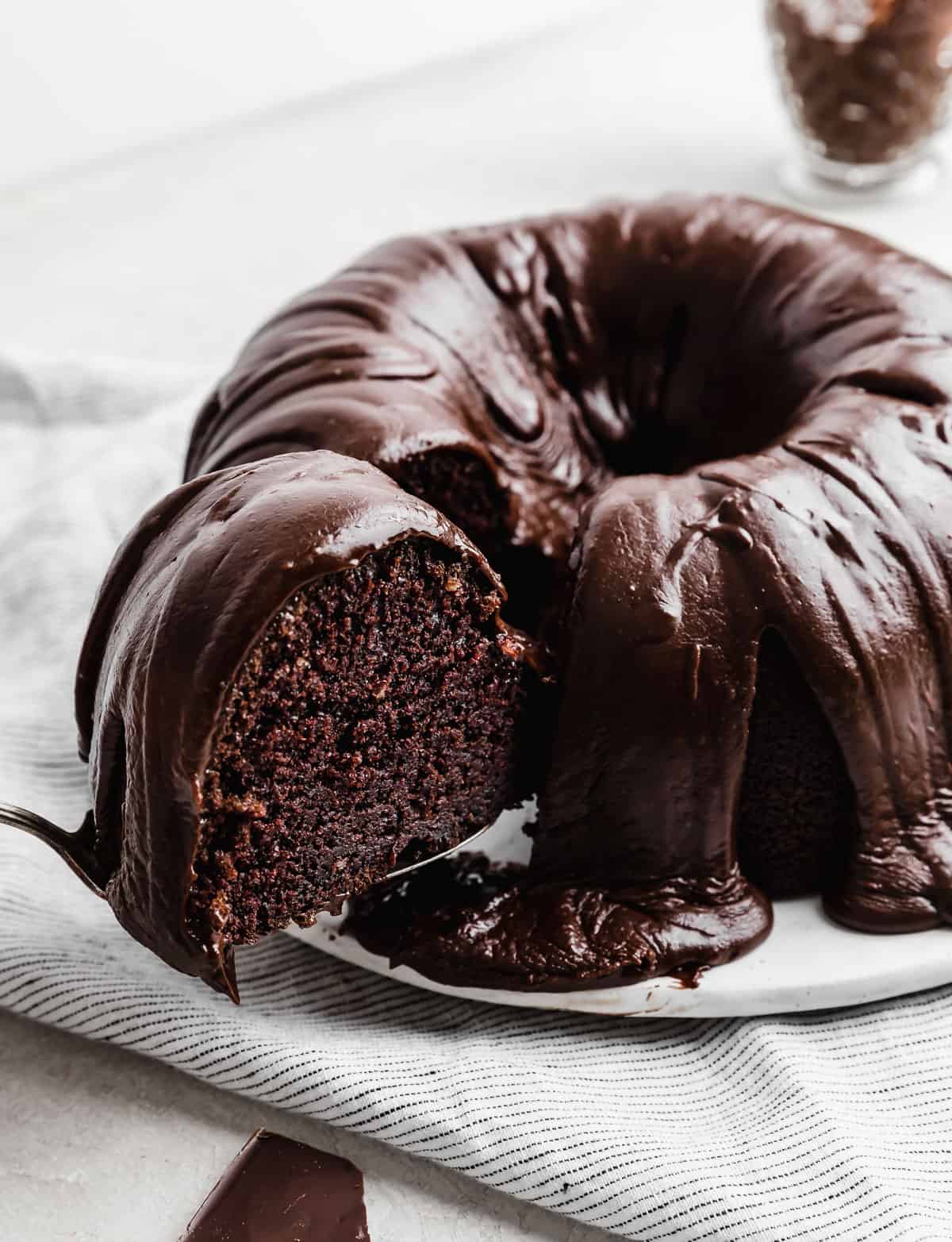 A chocolate glazed Chocolate Buttermilk Bundt Cake with a slice being removed from the cake.