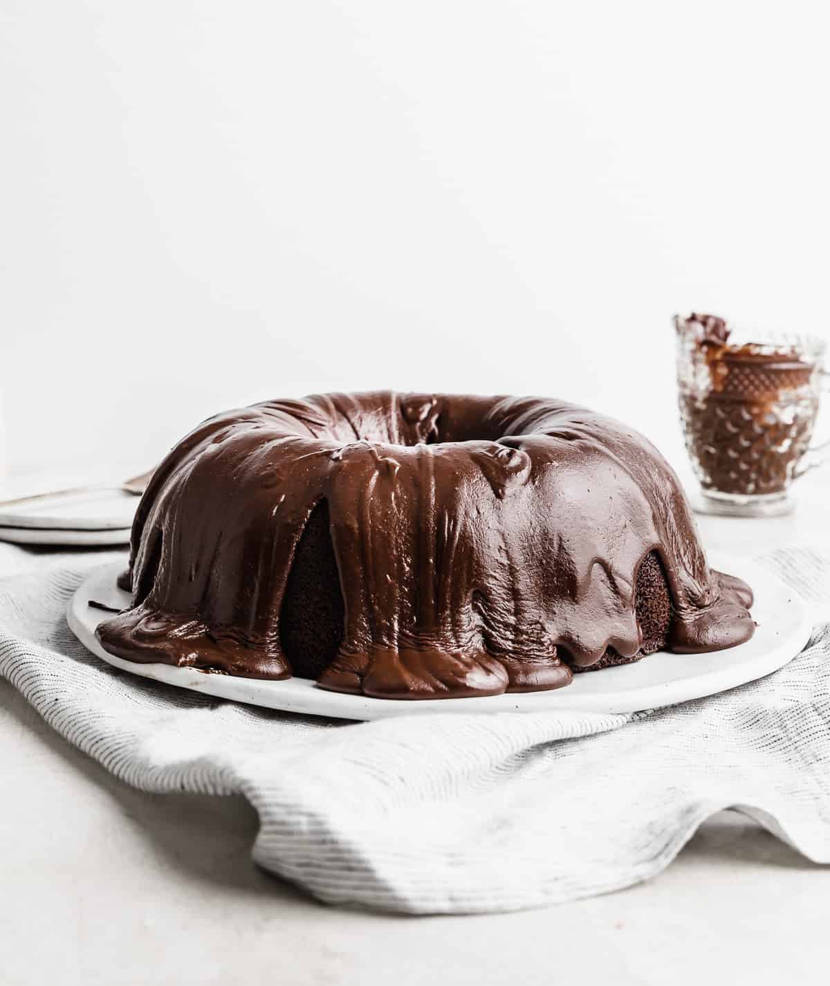 A chocolate frosting covered chocolate Bundt Cake on a white plate against a white background.