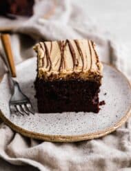 A slice of square chocolate cake topped with a peanut butter frosting and drizzled with melted chocolate.