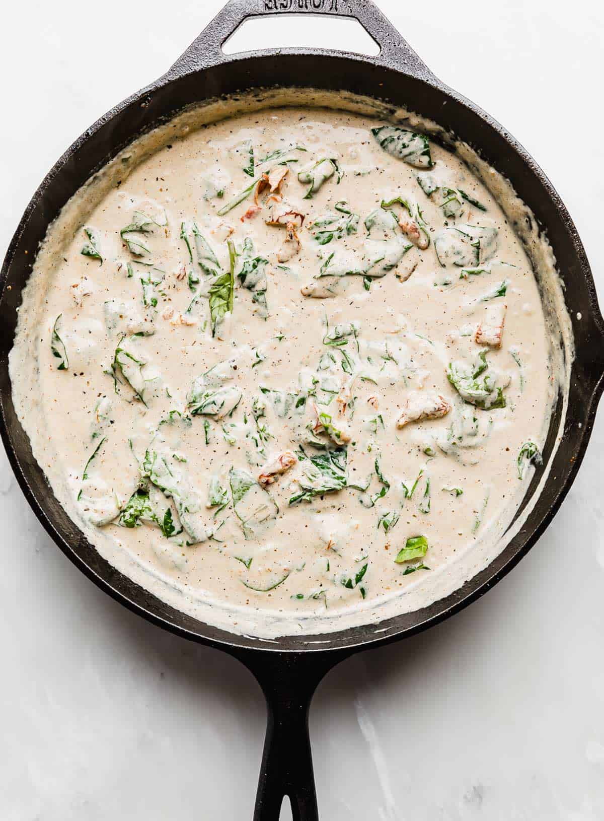 Creamy Tuscan Chicken gravy with spinach in a cast iron skillet.