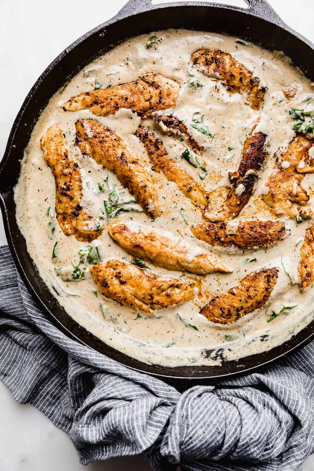 A black cast iron skillet full of a Creamy Tuscan Chicken Recipe swimming in a tan colored gravy.