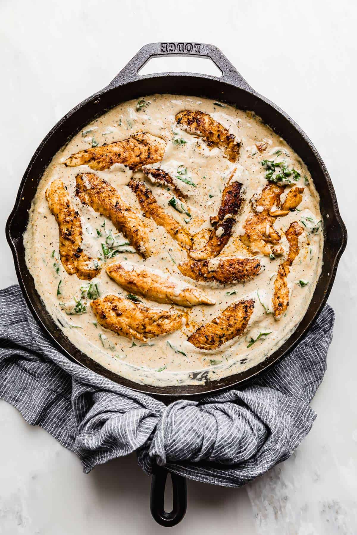 Creamy Tuscan Chicken Recipe in a skillet on a white background.
