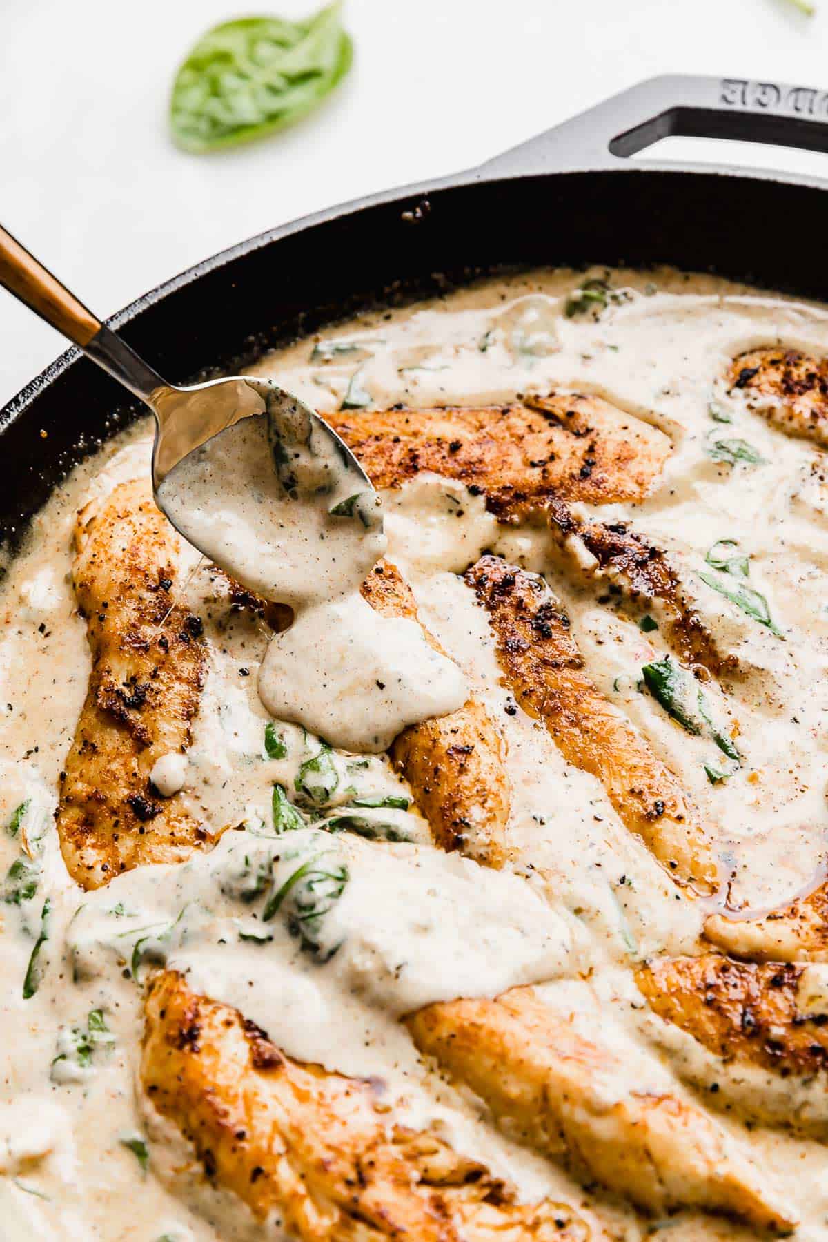 A spoon pouring a tuscan chicken gravy overtop chicken tender pieces in a skillet.
