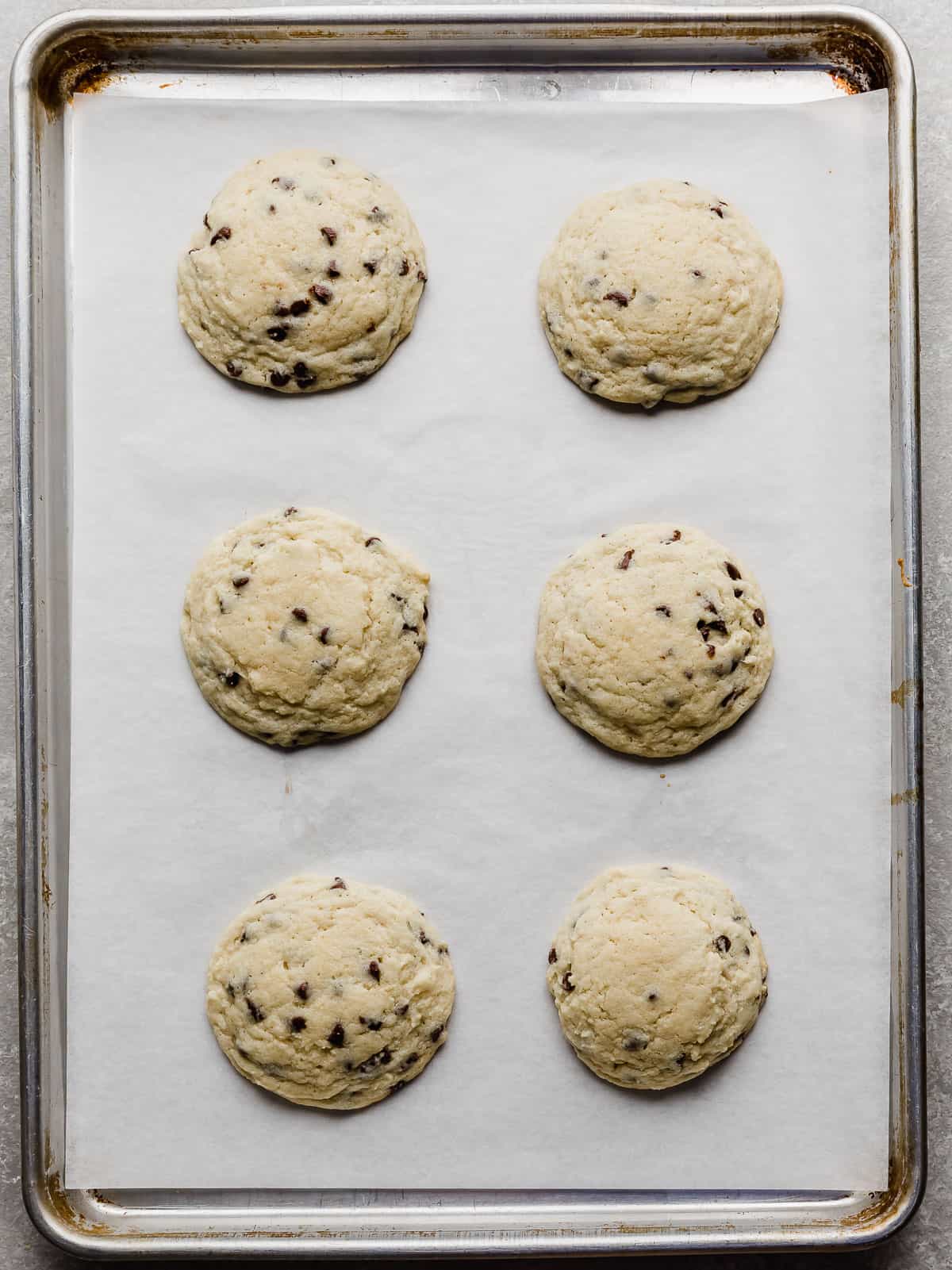 Six Mini chocolate chip studded sugar cookies on a white parchment lined baking sheet.