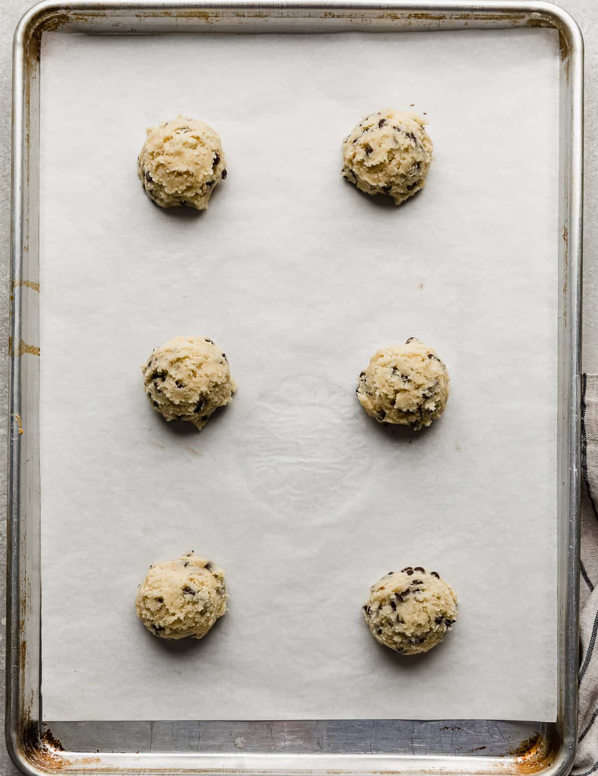 Six Crumbl Mint Chip Ice Cream Cookie dough balls on a white parchment lined baking sheet.