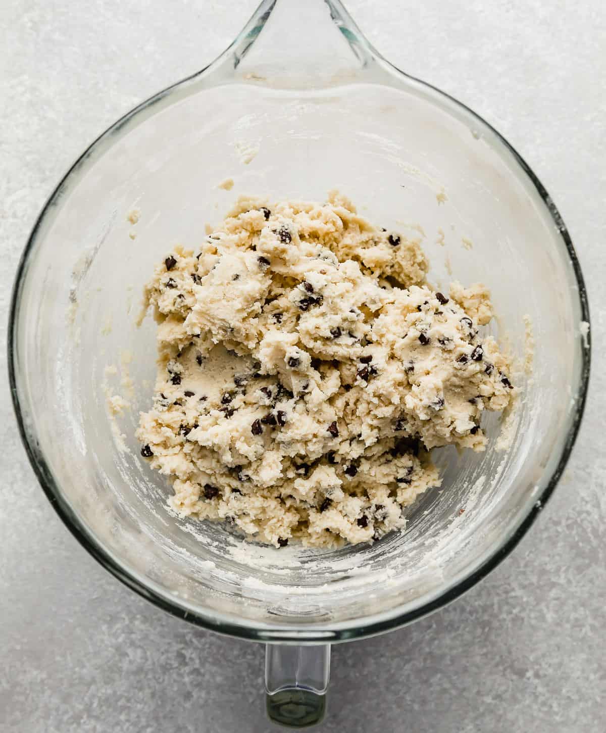 A glass mixing bowl with mini chocolate chips stirred into a sugar cookie dough.