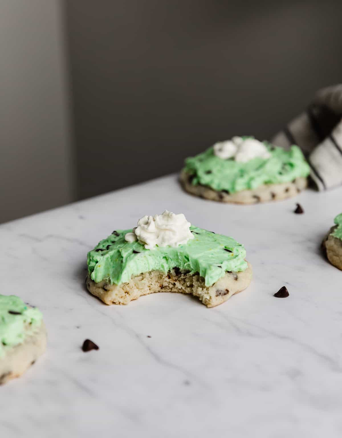 A Crumbl Mint Chip Ice Cream Cookie topped with a green frosting and dollop of whip cream on a white marble table.