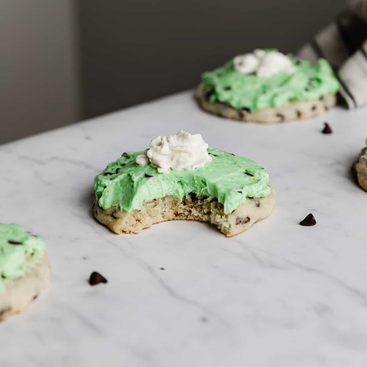 A bite taken out of a copycat Crumbl Mint Chip Ice Cream Cookie that's topped with mint green frosting and a dollop of whip cream.