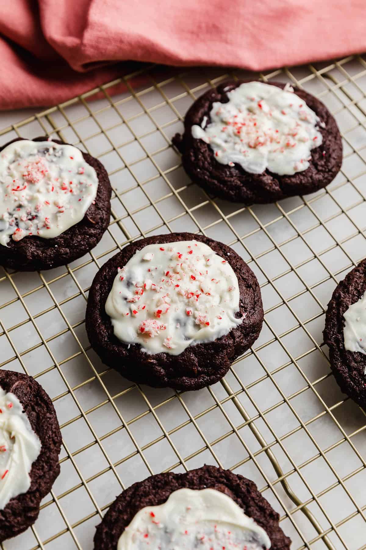 Crumbl Peppermint Bark Cookies topped with melted white chocolate and crushed candy canes on a gold wire rack.