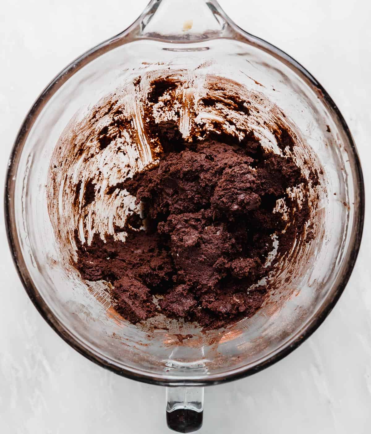 Chocolate peppermint cookie dough batter in a glass bowl on a white background.