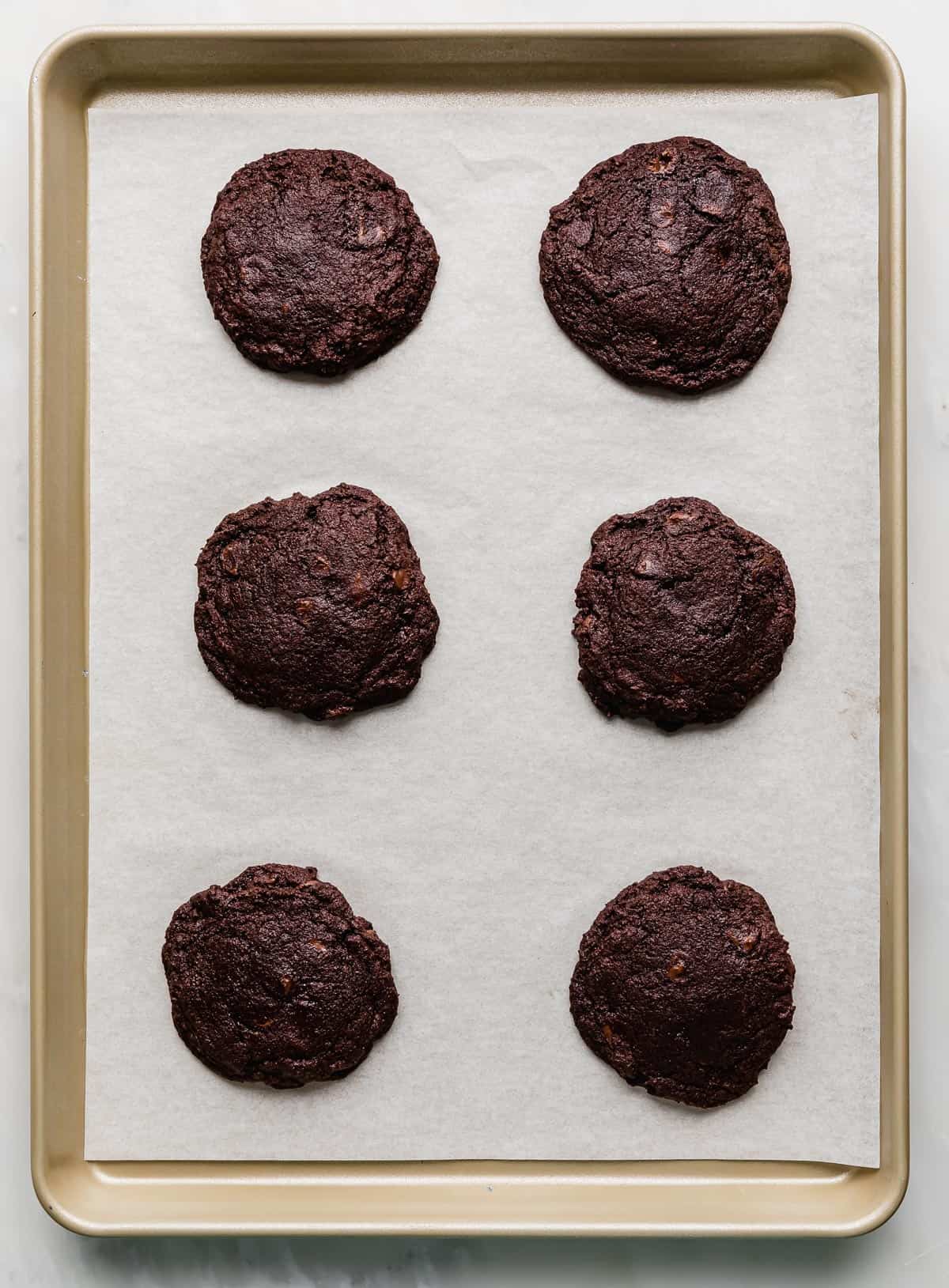 Six baked chocolate cookies on a white parchment lined baking sheet.