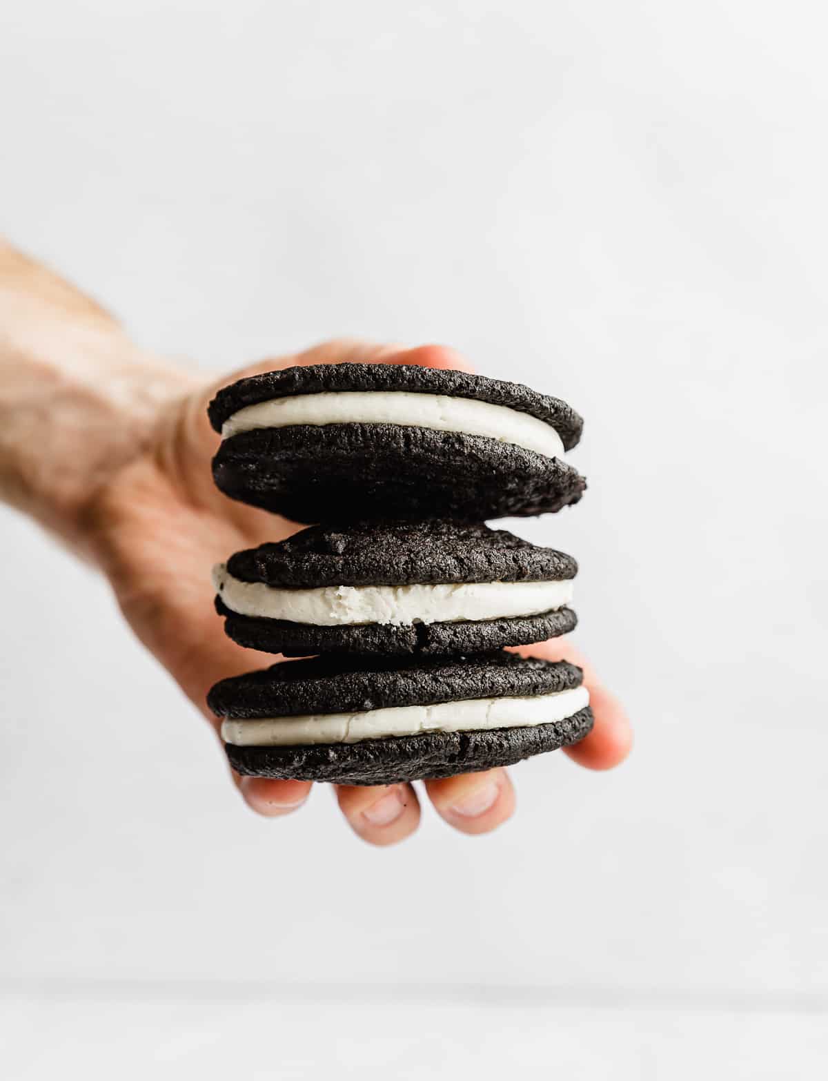 A single hand holding a stack of three Homemade Oreo Cookies sandwiched with a white vanilla frosting.