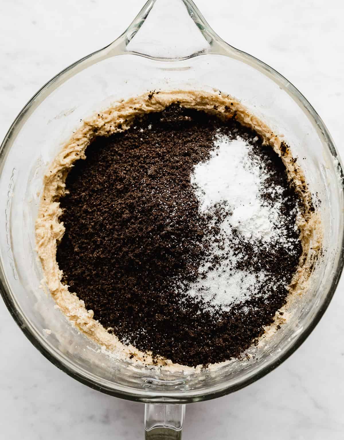 A glass bowl with black cocoa powder, crushed Oreos, salt, baking powder, and baking soda in it.