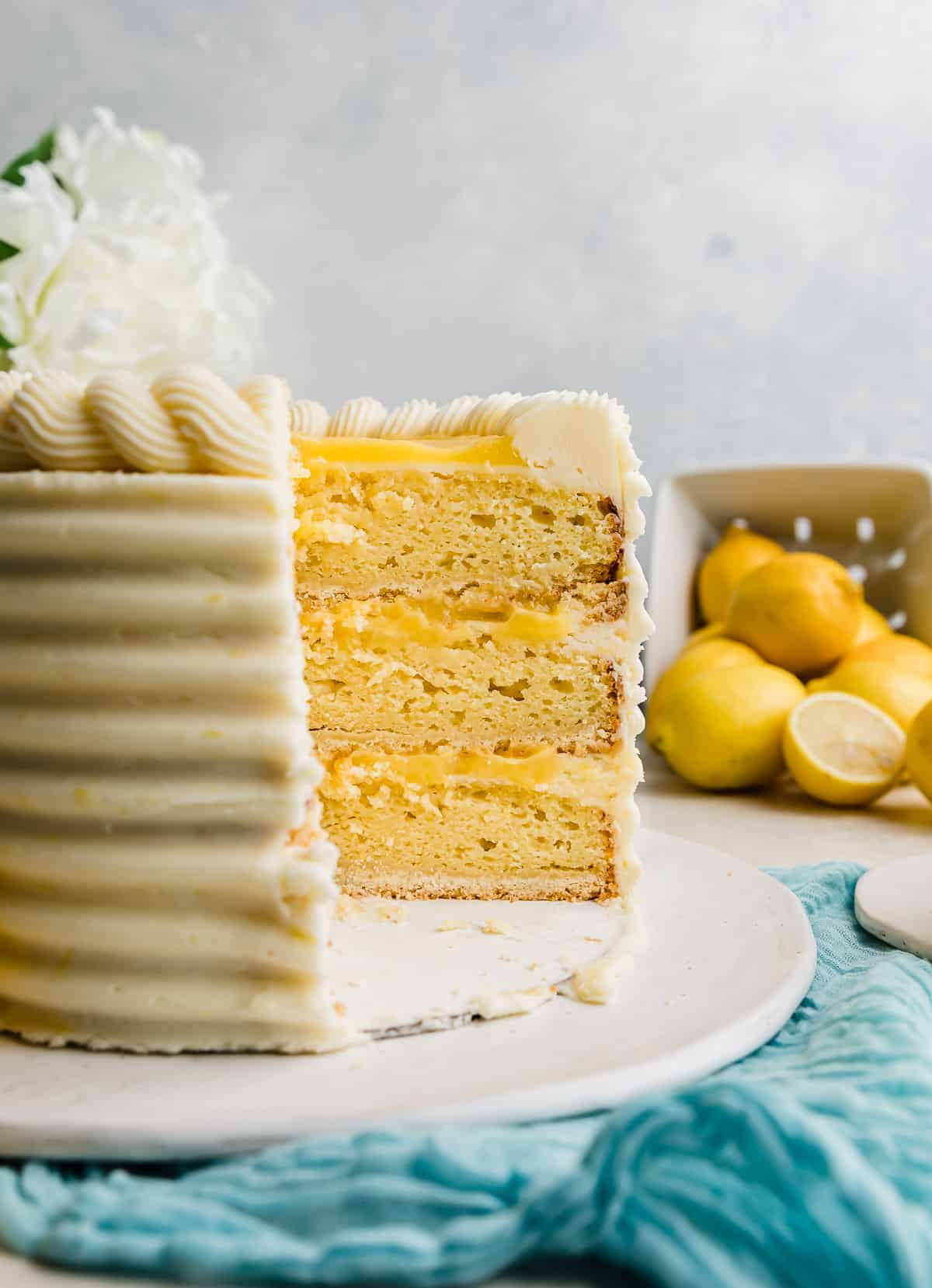A Lemon Bar Cake cut into showing the layers: shortbread crust, lemon cake, lemon curd, and lemon frosting.