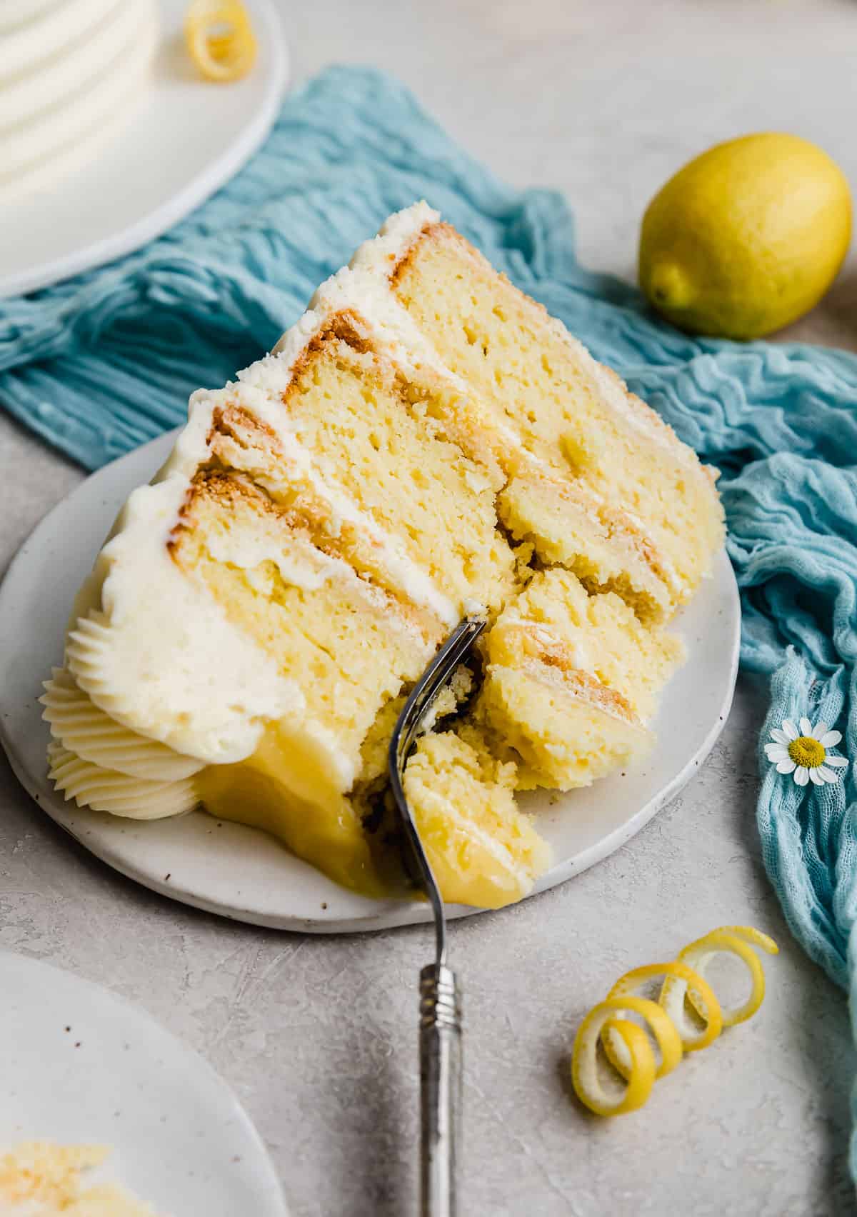A slice of layered Lemon Bar Cake on a plate with a fork cutting into the cake.
