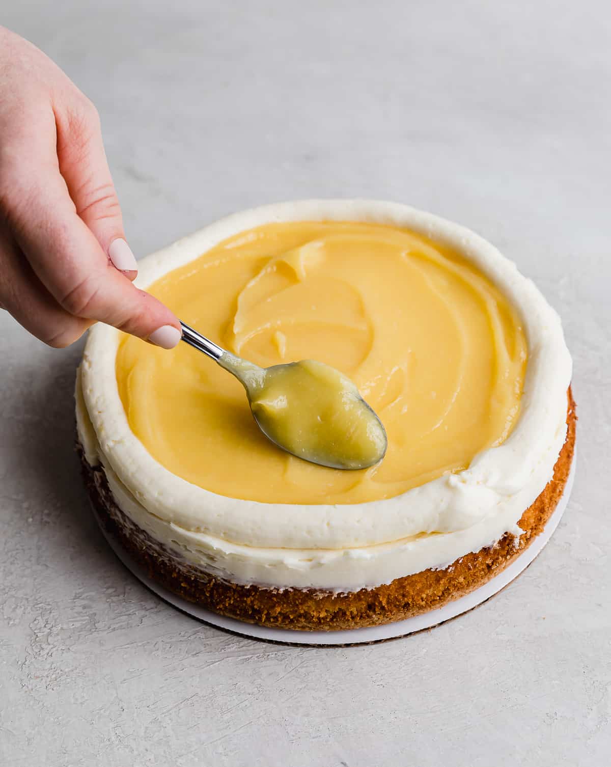 A spoon swirling the lemon curd on top of a Lemon Bar Cake.