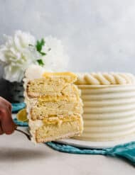A slice of lemon bar layer cake being held up in front of the full cake.