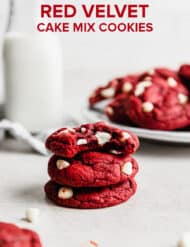 Three white chocolate chip studded Red Velvet Cake Mix Cookies stacked on top of each other, with the top cookie having a bite taken out of it.