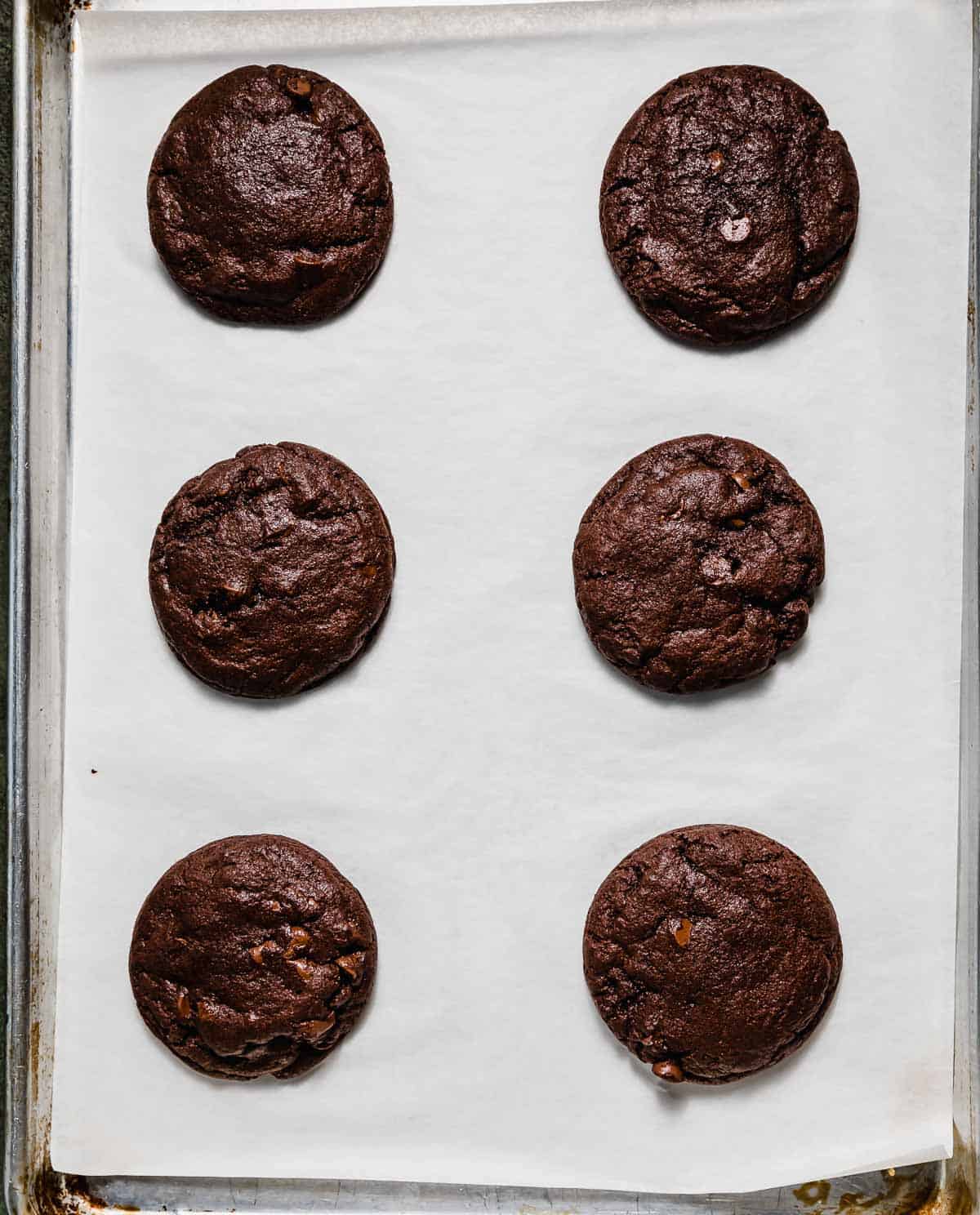 Six baked chocolate Peppermint Bark Cookies on a white parchment paper.