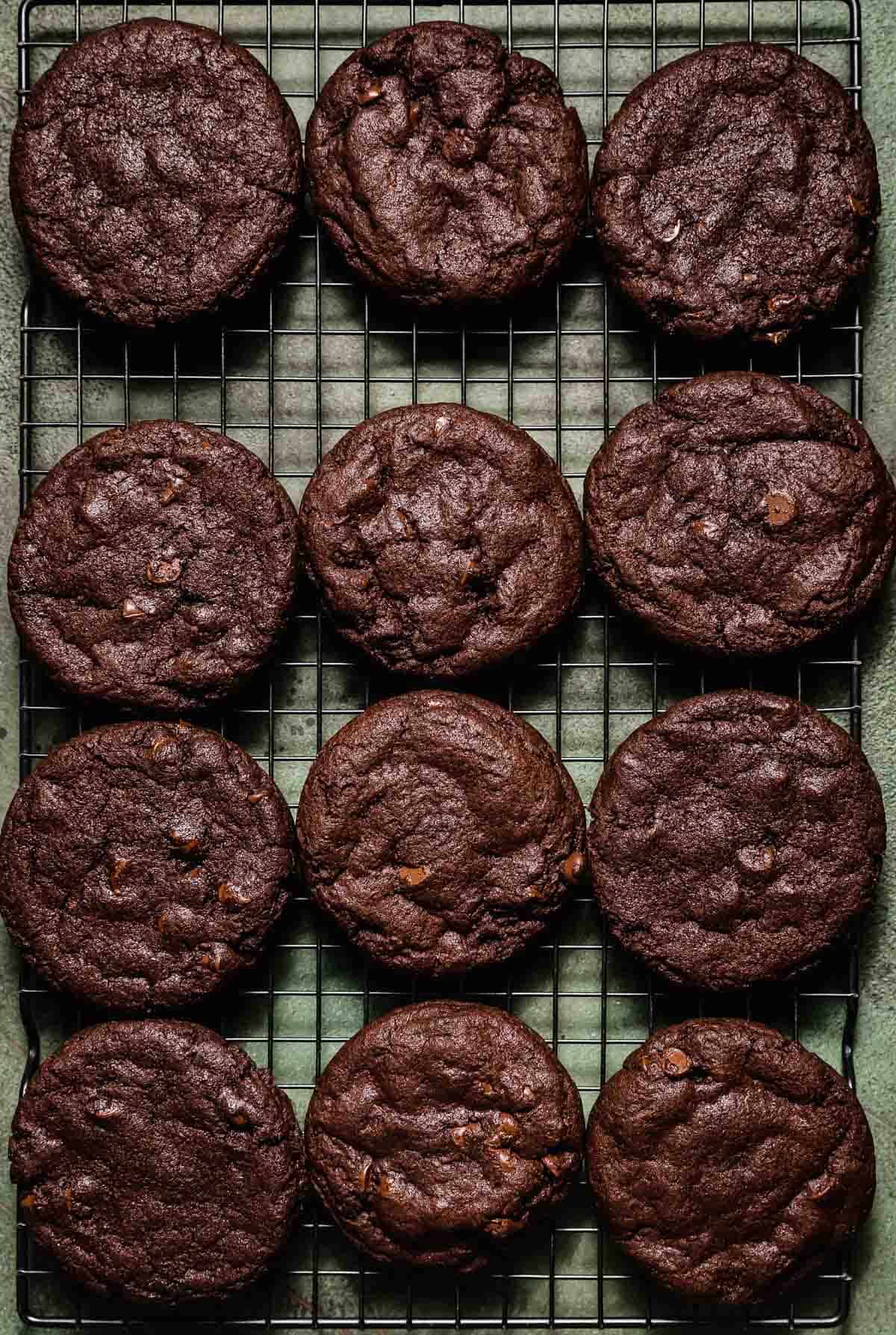 Chocolate cookies on a black wire cooling rack on a green background. 