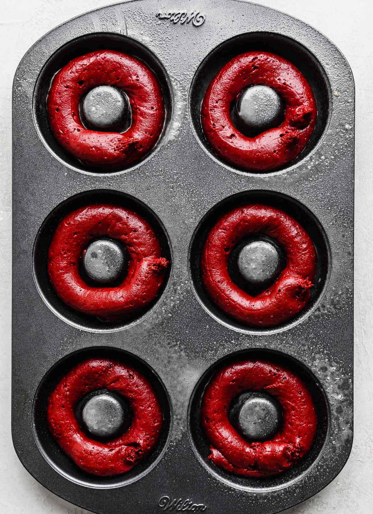 A donut pan with red velvet donut batter in the donut cavities.