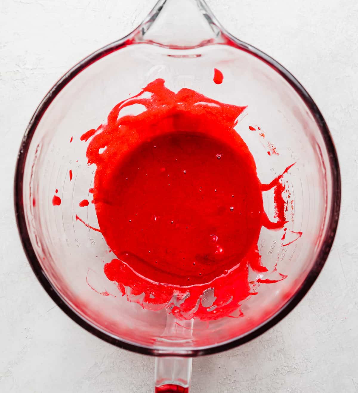 A bright red colored wet ingredients batter in a glass bowl.