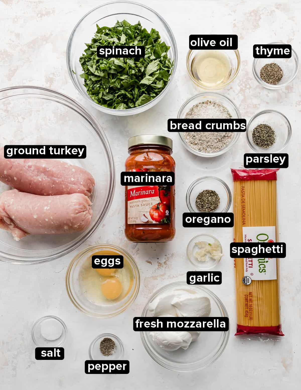 Ingredients used to make Turkey Spinach Meatballs and Spaghetti portioned into glass bowls placed on a white background.