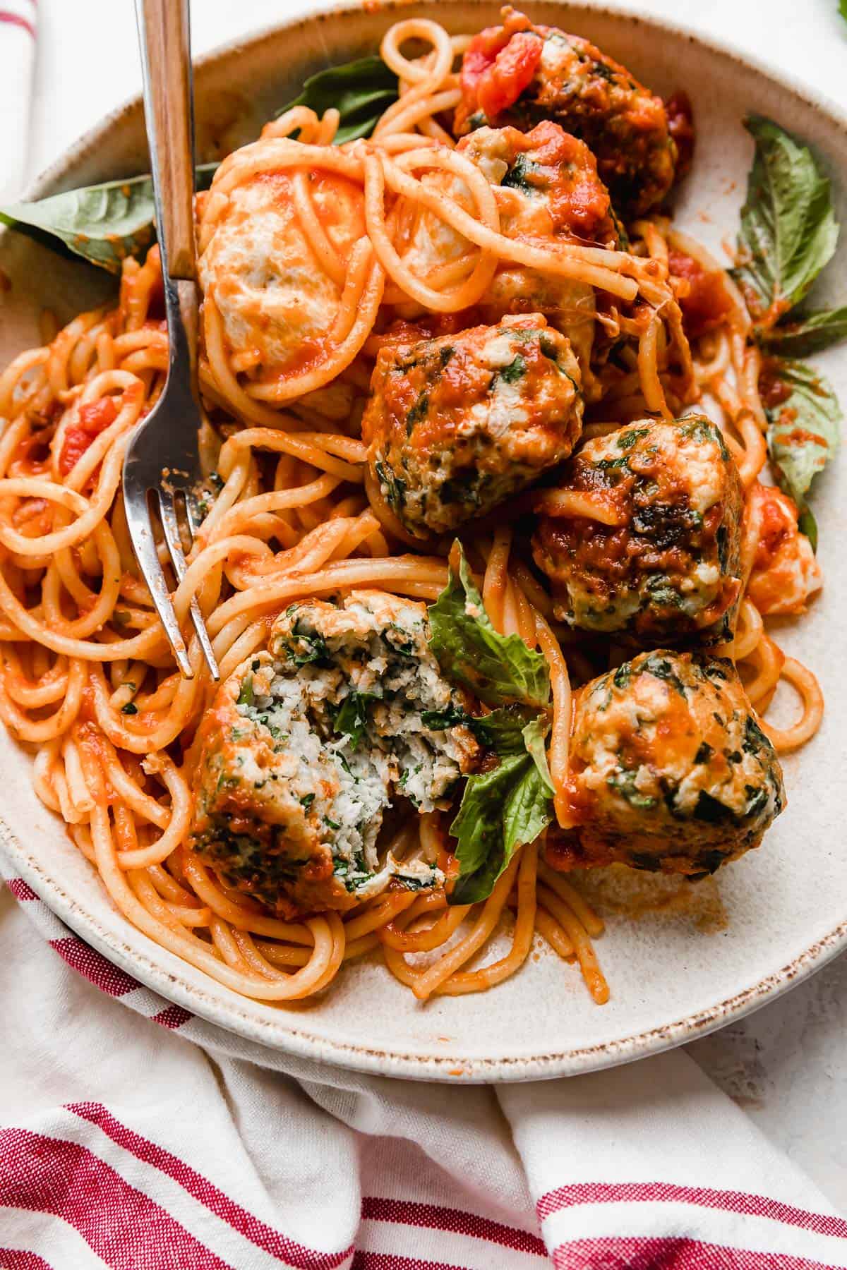 A close up photo of a turkey spinach meatballs atop spaghetti noodles.