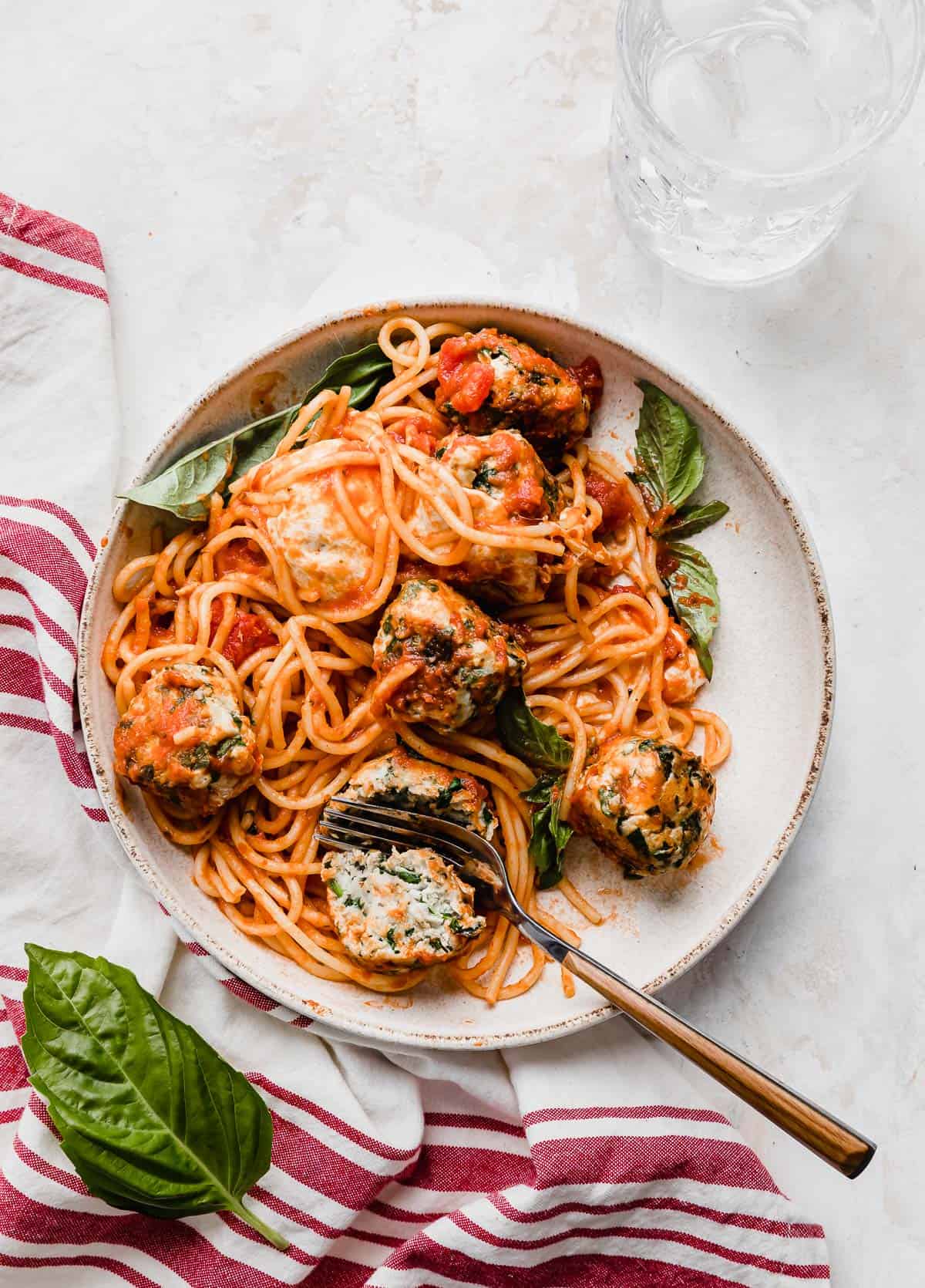 Turkey Spinach Meatballs and Spaghetti on a white plate with a red striped towel to the left side of the plate.